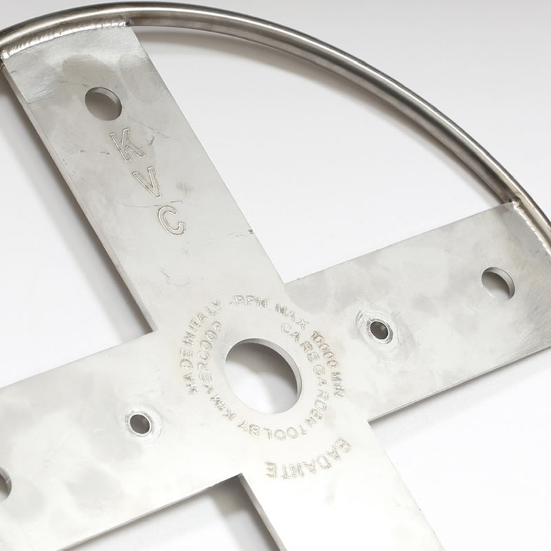 Close-up of a metal Kimvercoop Badante garden tool part. Features include a ring, cross shape, and various engravings.
